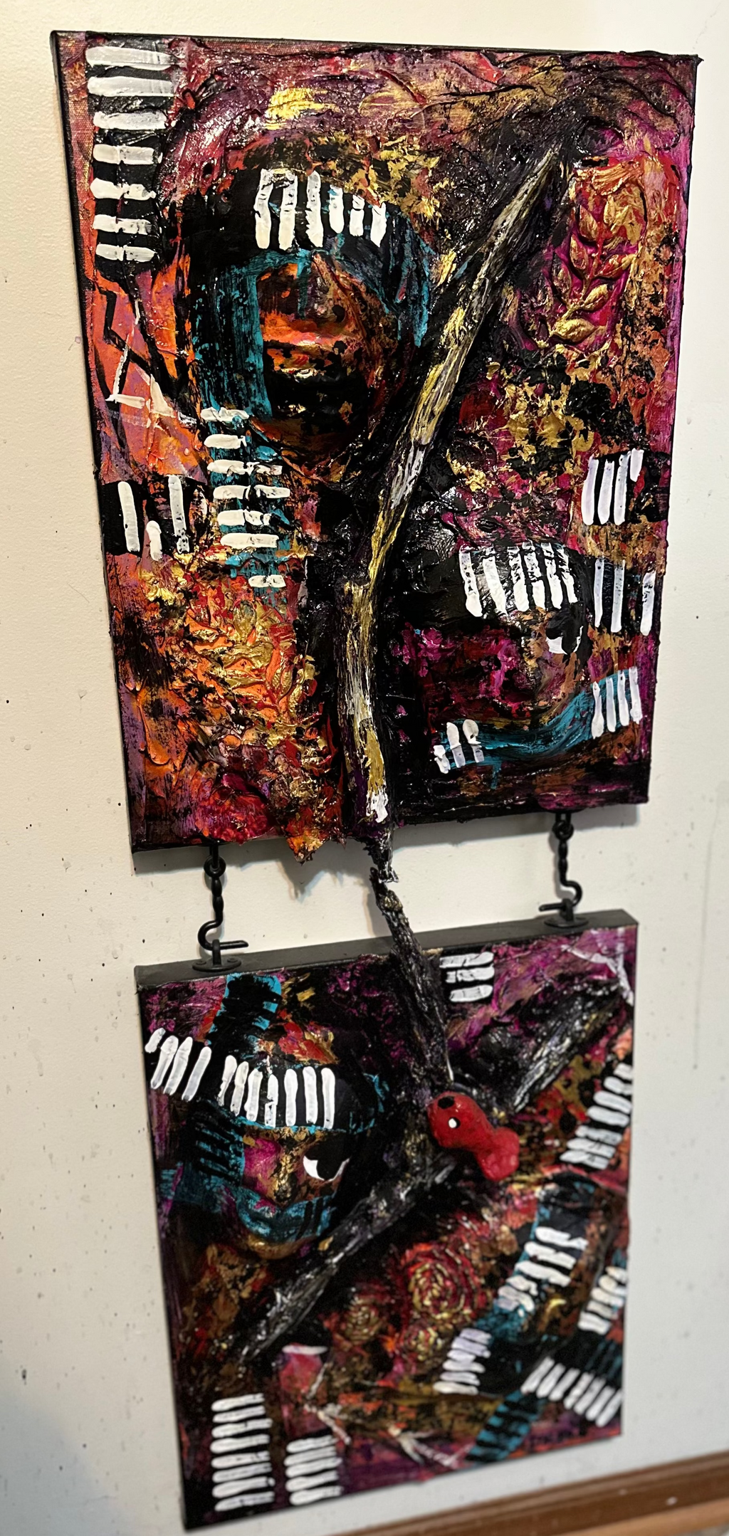 Two abstract art pieces hanging on a wall with a power outlet in the background.